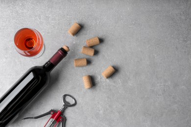 Photo of Wine corks, bottle, glass of drink and corkscrew on light grey table, flat lay. Space for text