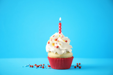 Delicious birthday cupcake with candle on light blue background