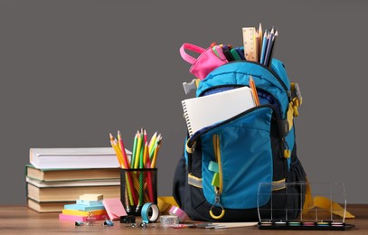 Backpack with different school stationery on wooden table near blackboard, space for text