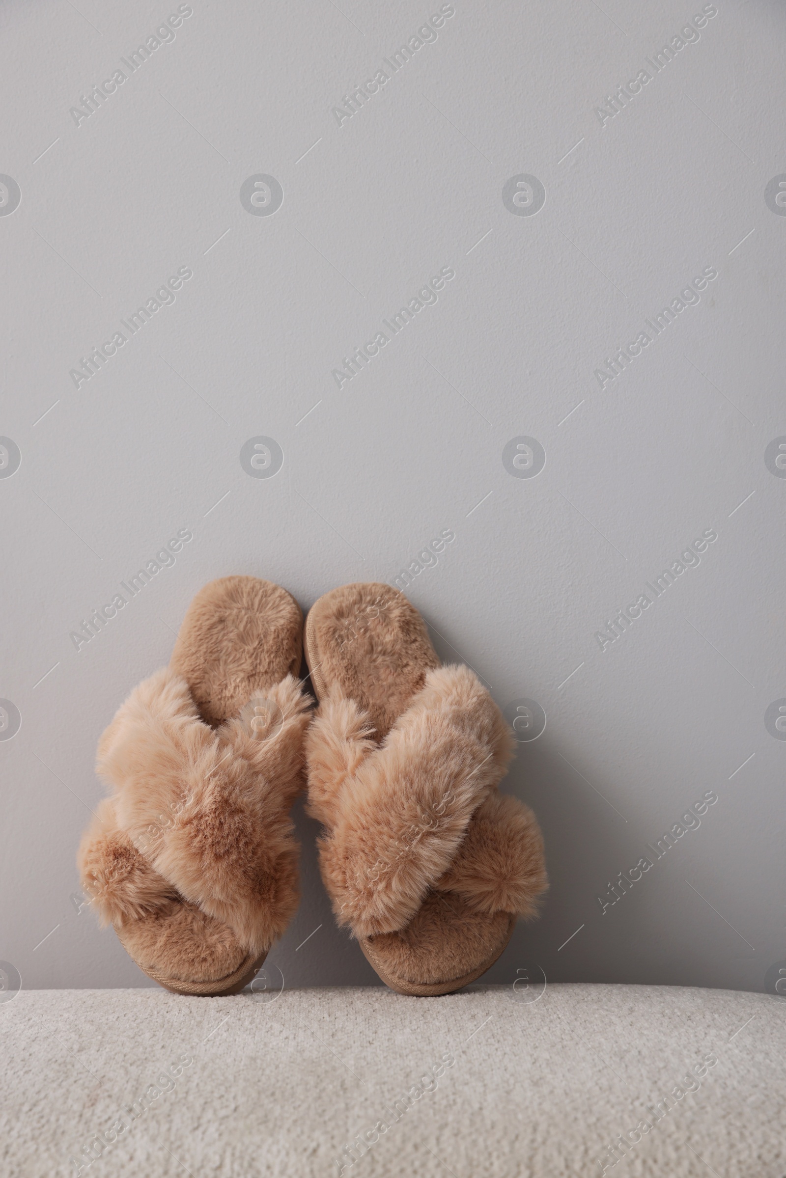 Photo of Soft beige slippers near grey wall, space for text