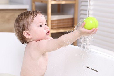 Photo of Cute little child playing with ball in bathtub at home