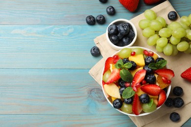 Photo of Tasty fruit salad in bowl and ingredients on light blue wooden table, flat lay. Space for text