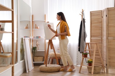 Photo of Beautiful young woman drawing on easel at home