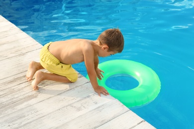 Little child reaching for inflatable ring in outdoor swimming pool. Dangerous situation