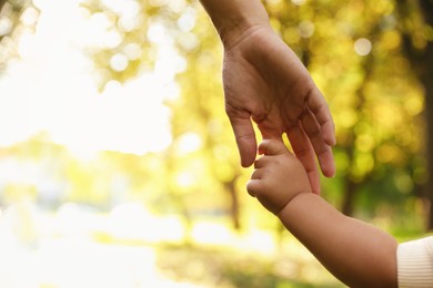 Daughter holding mother's hand outdoors, closeup. Happy family