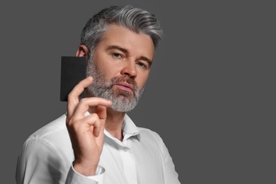 Handsome man holding blank business card on grey background. Space for text