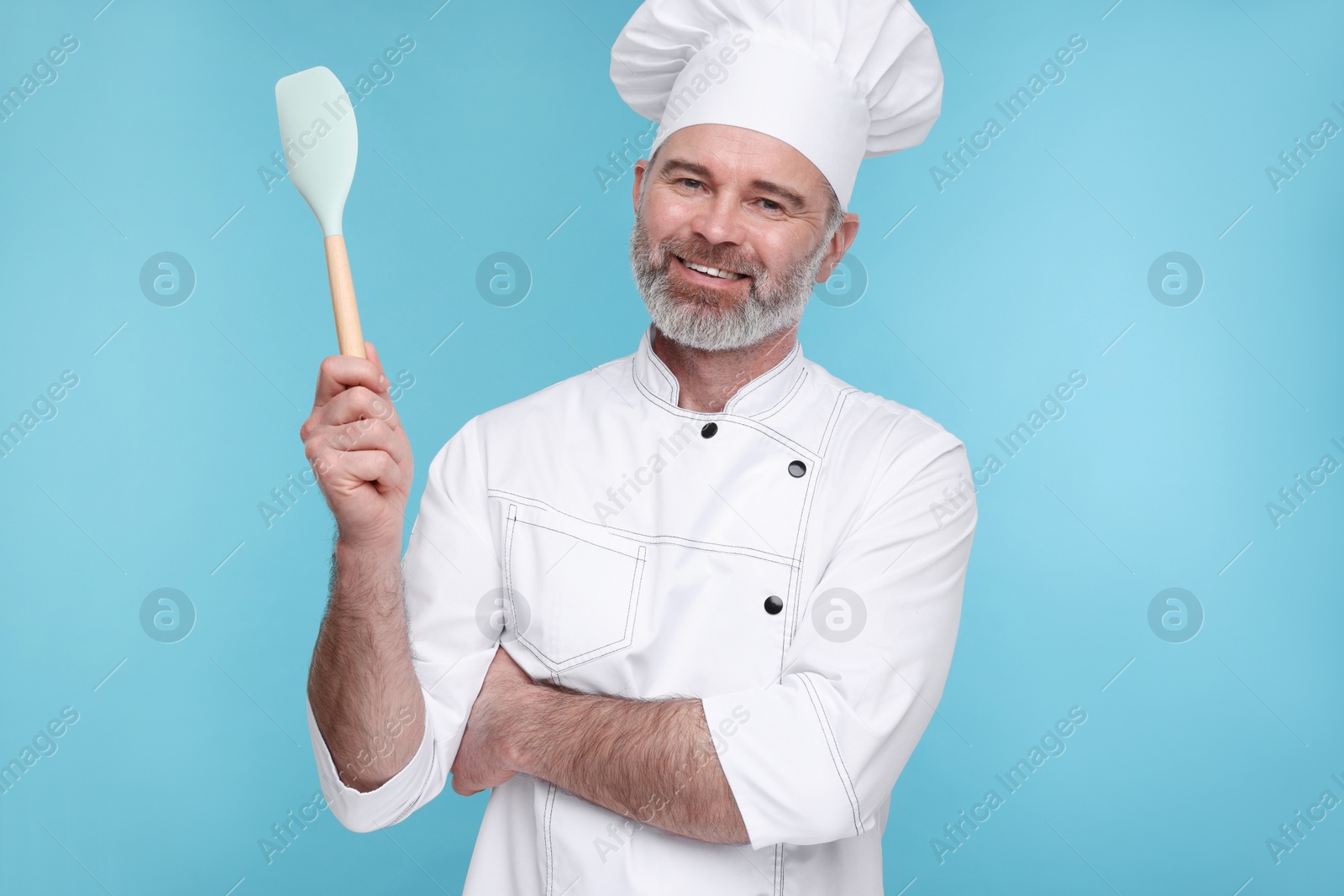 Photo of Happy chef in uniform with spatula on light blue background