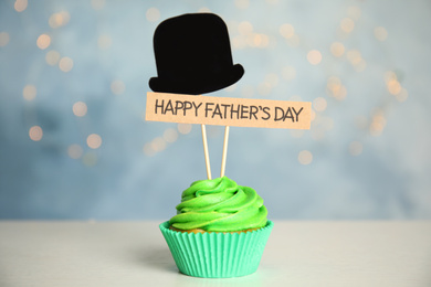 Photo of Cupcake with paper hat and HAPPY FATHER'S DAY tag on white table against blurred background