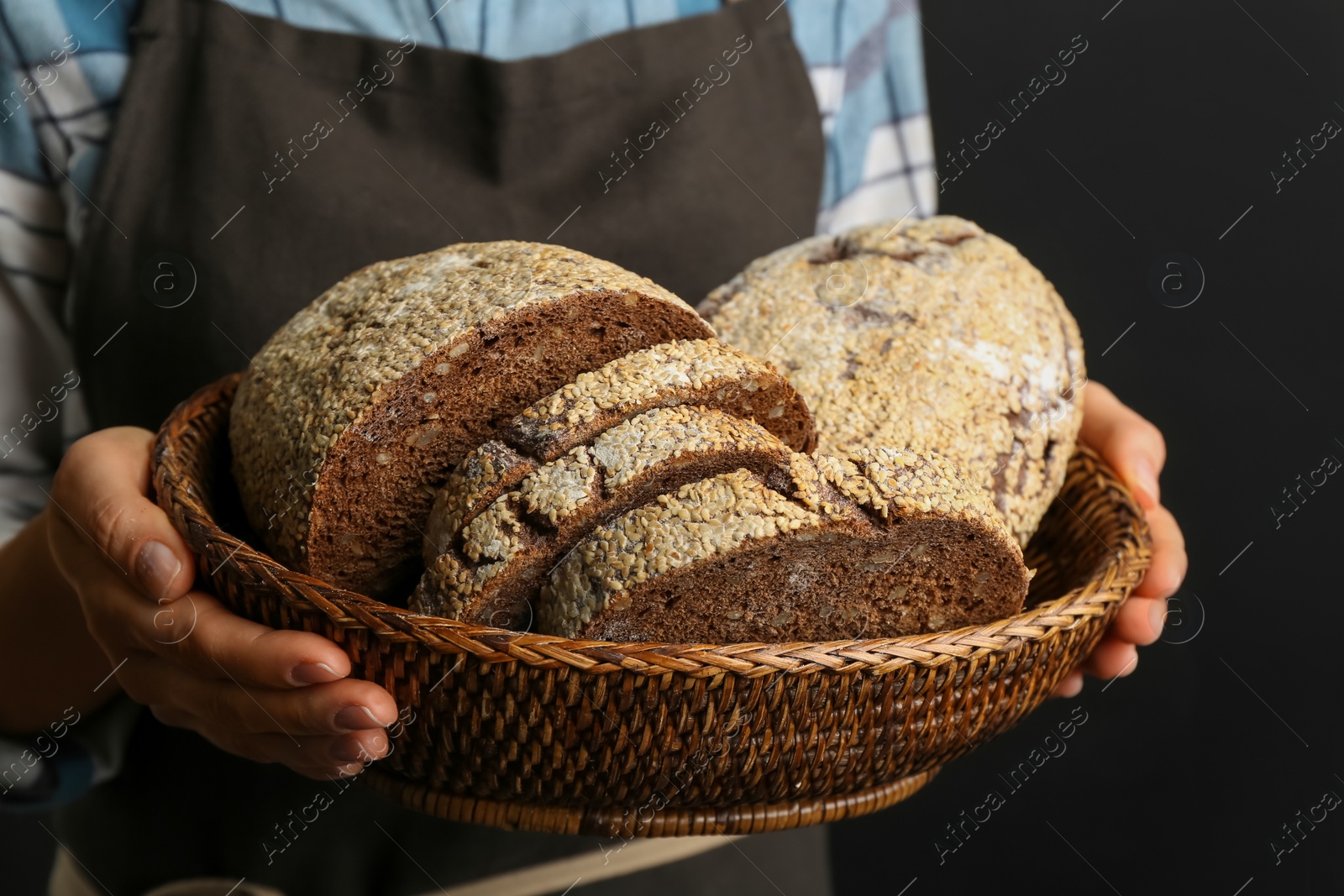 Photo of Woman holding freshly baked bread on black background, closeup