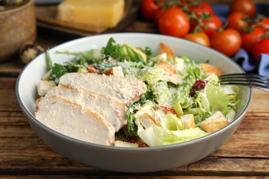 Photo of Delicious Caesar salad in bowl on wooden table, closeup