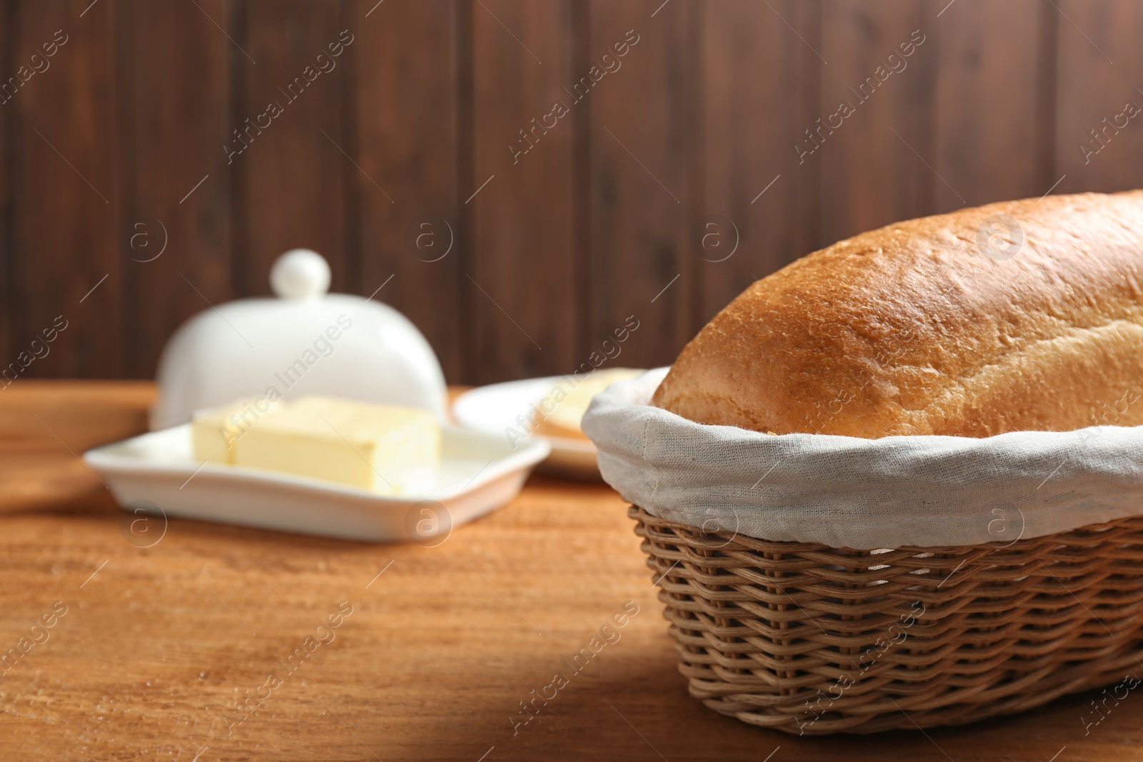 Photo of Loaf of tasty fresh bread in wicker basket on wooden table, closeup. Space for text