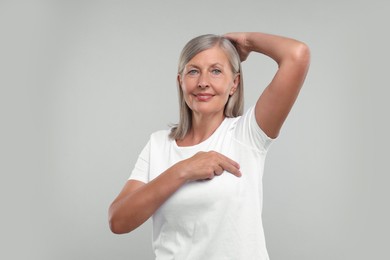 Photo of Beautiful senior woman doing breast self-examination on light grey background