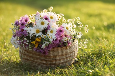 Photo of Wicker basket with beautiful wild flowers on green grass outdoors