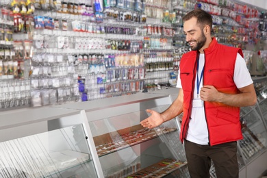 Photo of Salesman standing near showcase with fishing equipment in sports shop. Space for text