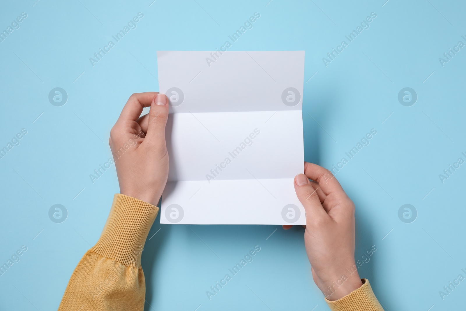 Photo of Woman with blank sheet of paper at light blue table, top view. Space for text