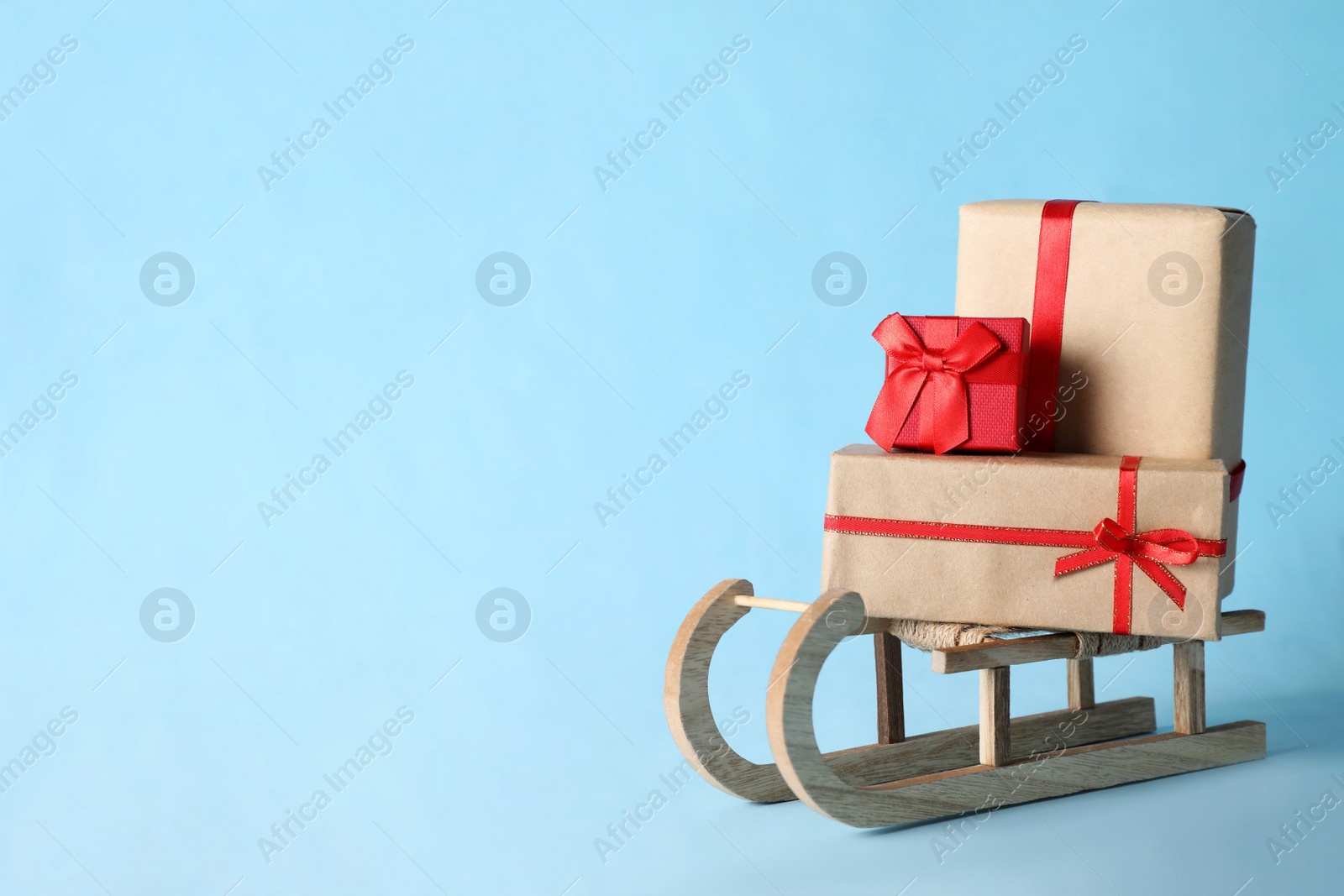 Photo of Wooden sleigh with Christmas gift boxes on light blue background, space for text