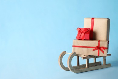 Photo of Wooden sleigh with Christmas gift boxes on light blue background, space for text