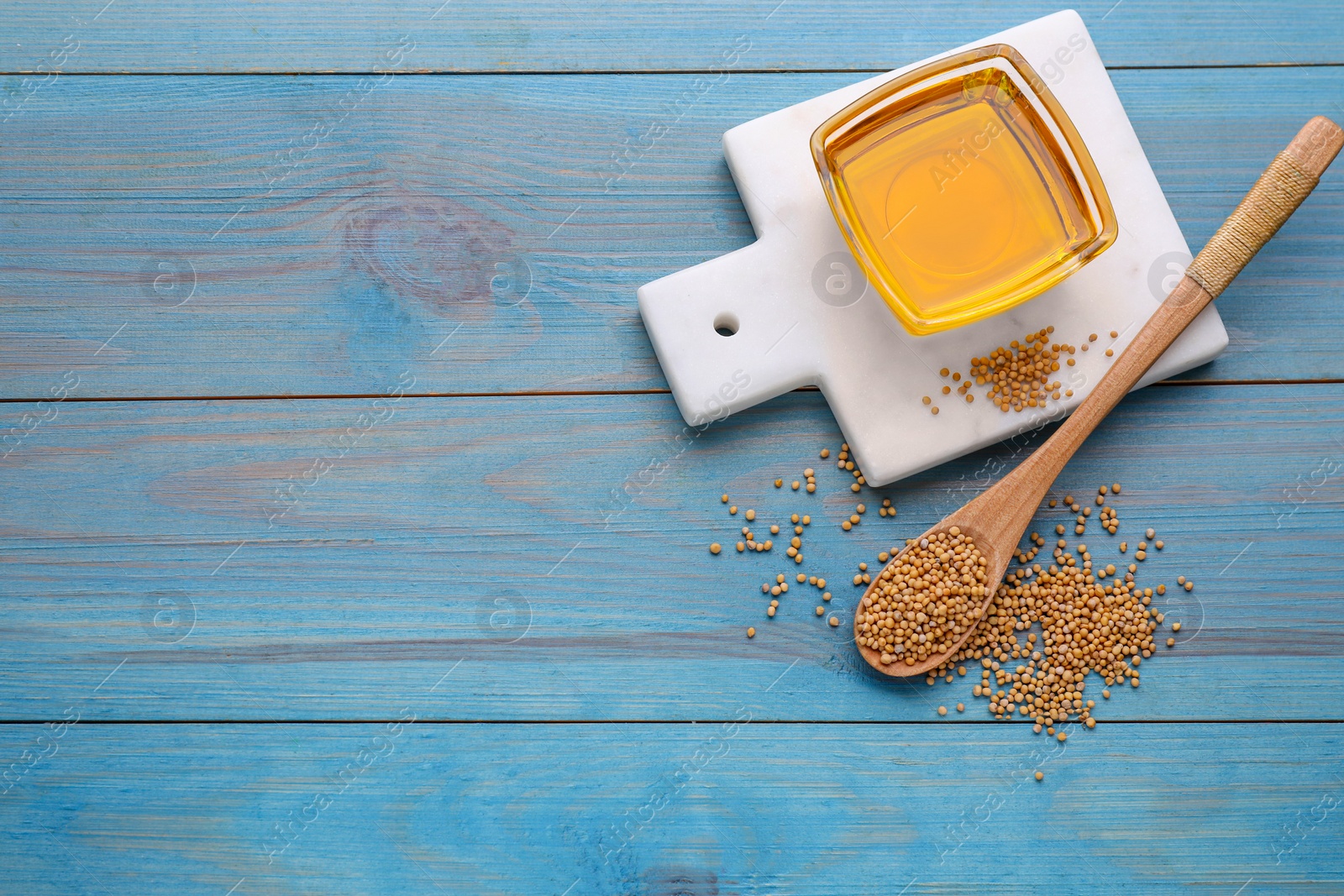 Bowl of natural oil and mustard seeds on light blue wooden table, flat lay. Space for text Photo of Bowl of natural oil and mustard seeds on light blue wooden table, flat lay. Space for text