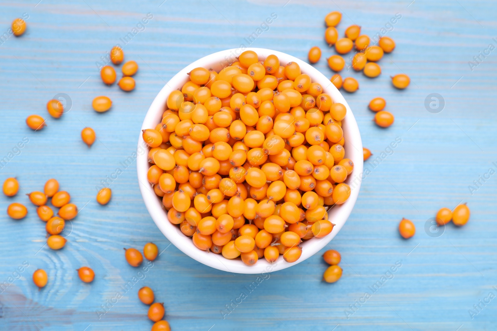 Photo of Bowl with fresh ripe sea buckthorn berries on light blue wooden table, flat lay