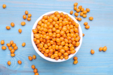 Bowl with fresh ripe sea buckthorn berries on light blue wooden table, flat lay