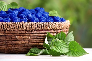 Image of Many fresh blue raspberries in wicker bowl on table, closeup