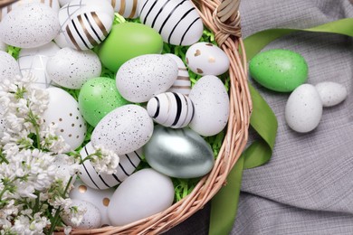 Photo of Easter eggs in basket and lilac flowers on table, flat lay