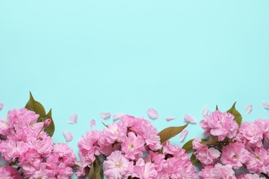 Photo of Beautiful sakura tree blossoms on turquoise background, flat lay. Space for text