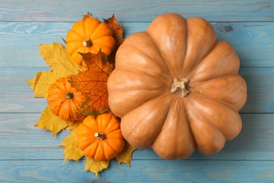 Photo of Fresh ripe pumpkins and dry leaves on turquoise wooden table, flat lay