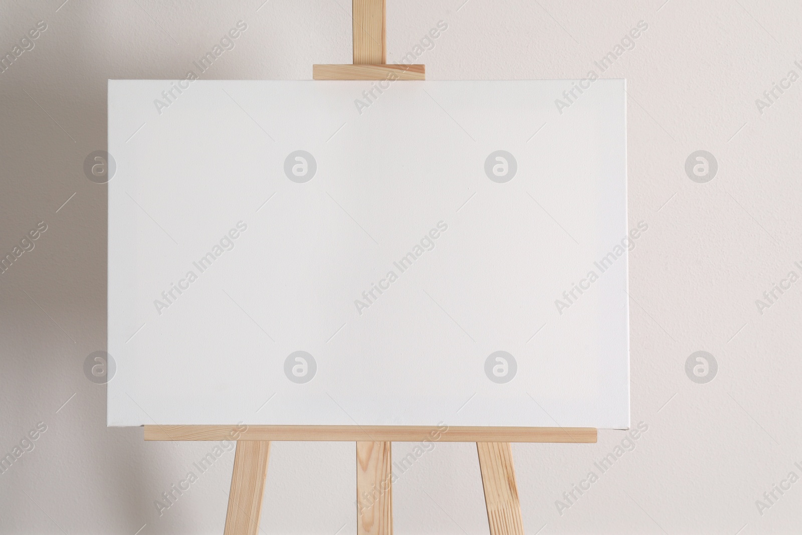 Photo of Wooden easel with blank canvas on light background
