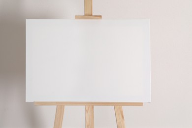 Photo of Wooden easel with blank canvas on light background