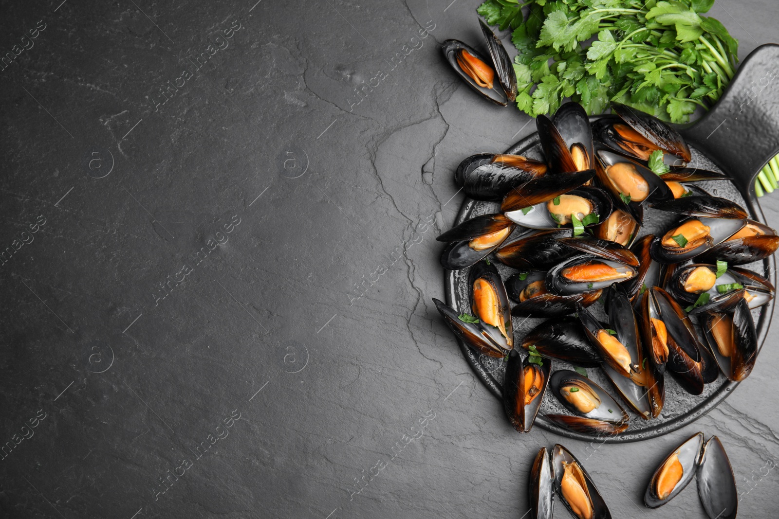 Photo of Serving board with cooked mussels and parsley on slate table, flat lay. Space for text