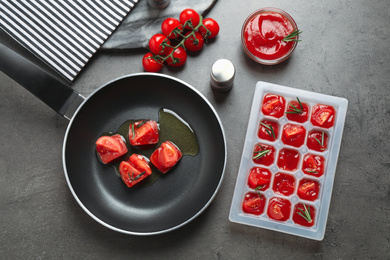 Flat lay composition of melting ice cubes with tomatoes, oil and rosemary on grey table