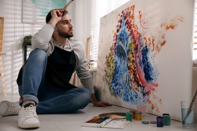 Photo of Young man painting on canvas with brush in artist studio