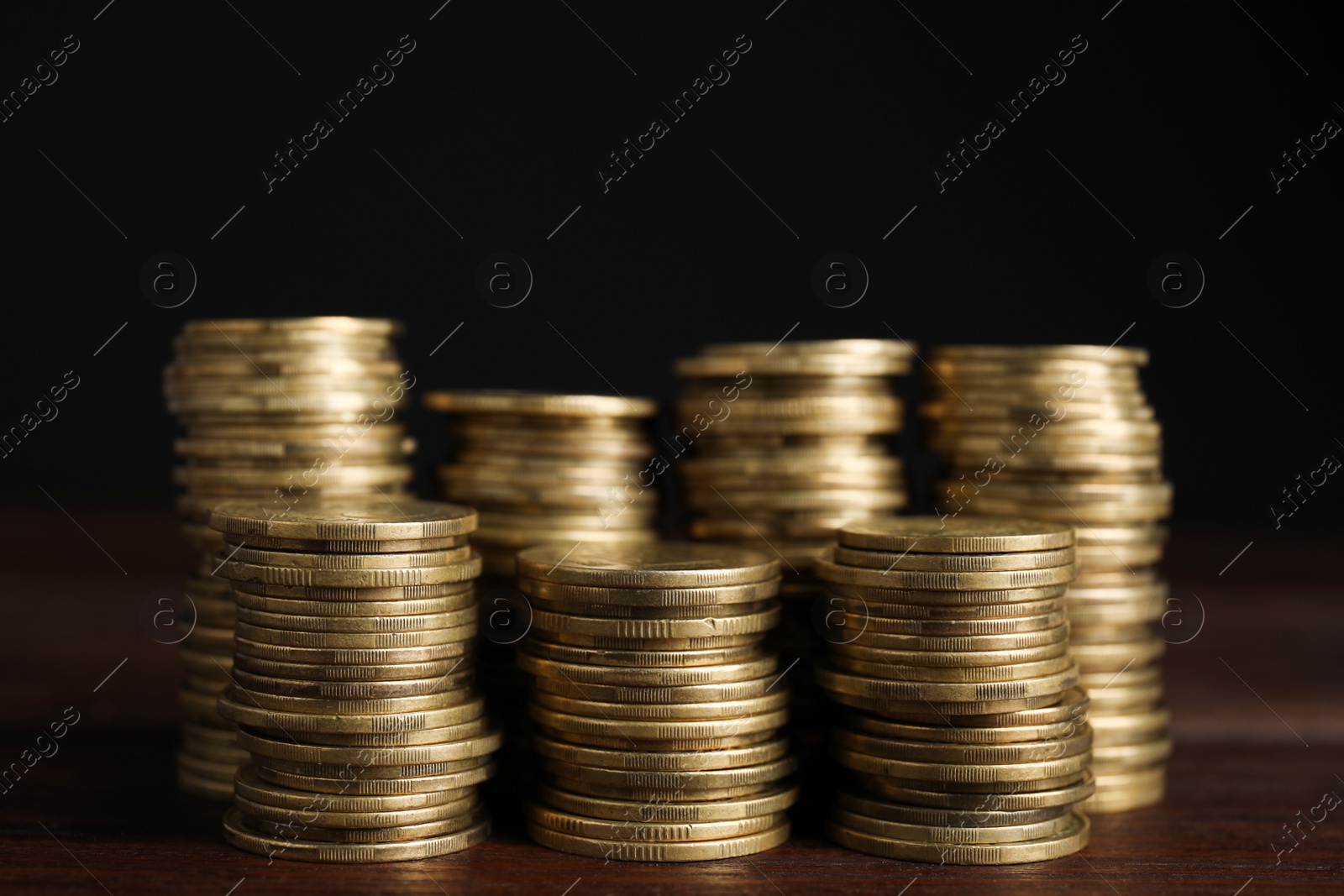 Photo of Many coins stacked on wooden table against black background