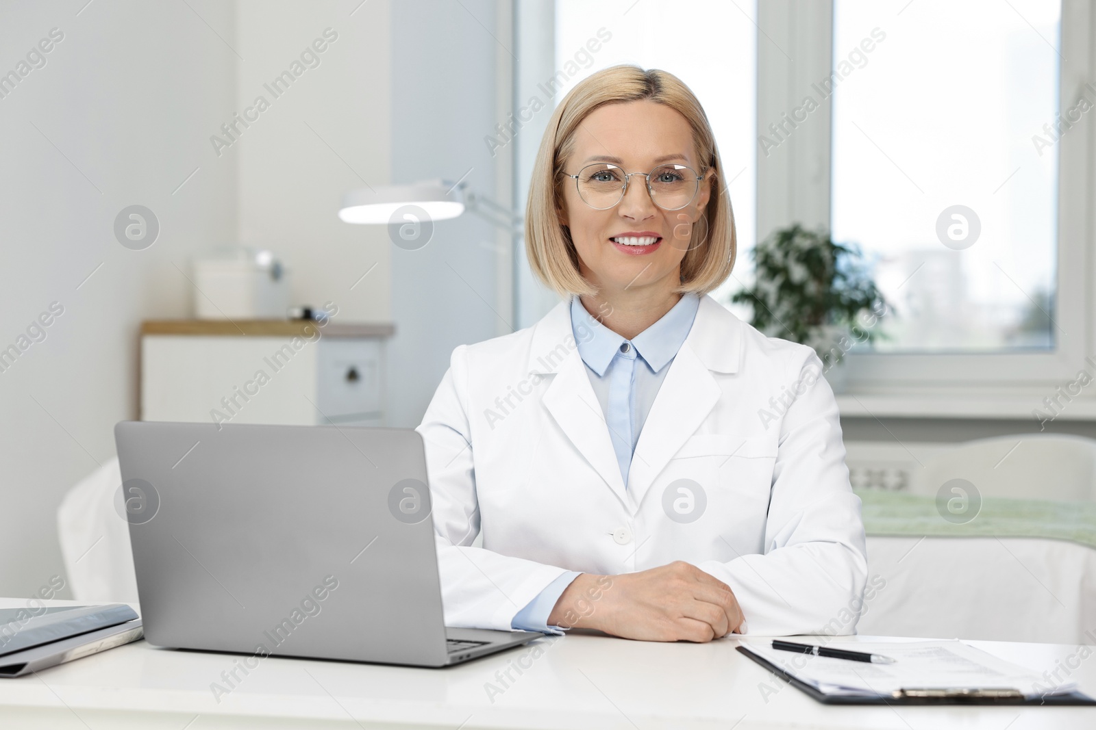 Photo of Portrait of happy dermatologist at white table in clinic