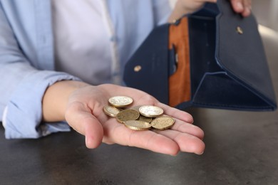 Poor woman holding coins and empty wallet at grey table indoors, closeup