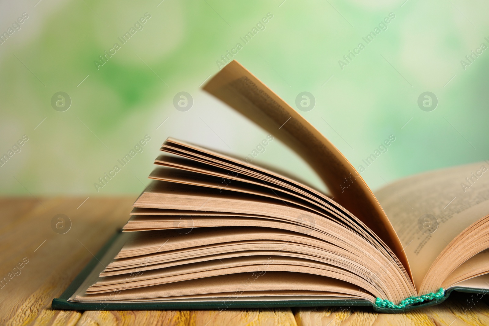 Photo of Open book on wooden table against blurred green background, closeup