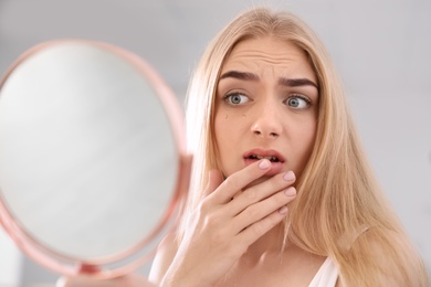 Young woman with eyelash loss problem looking in mirror indoors