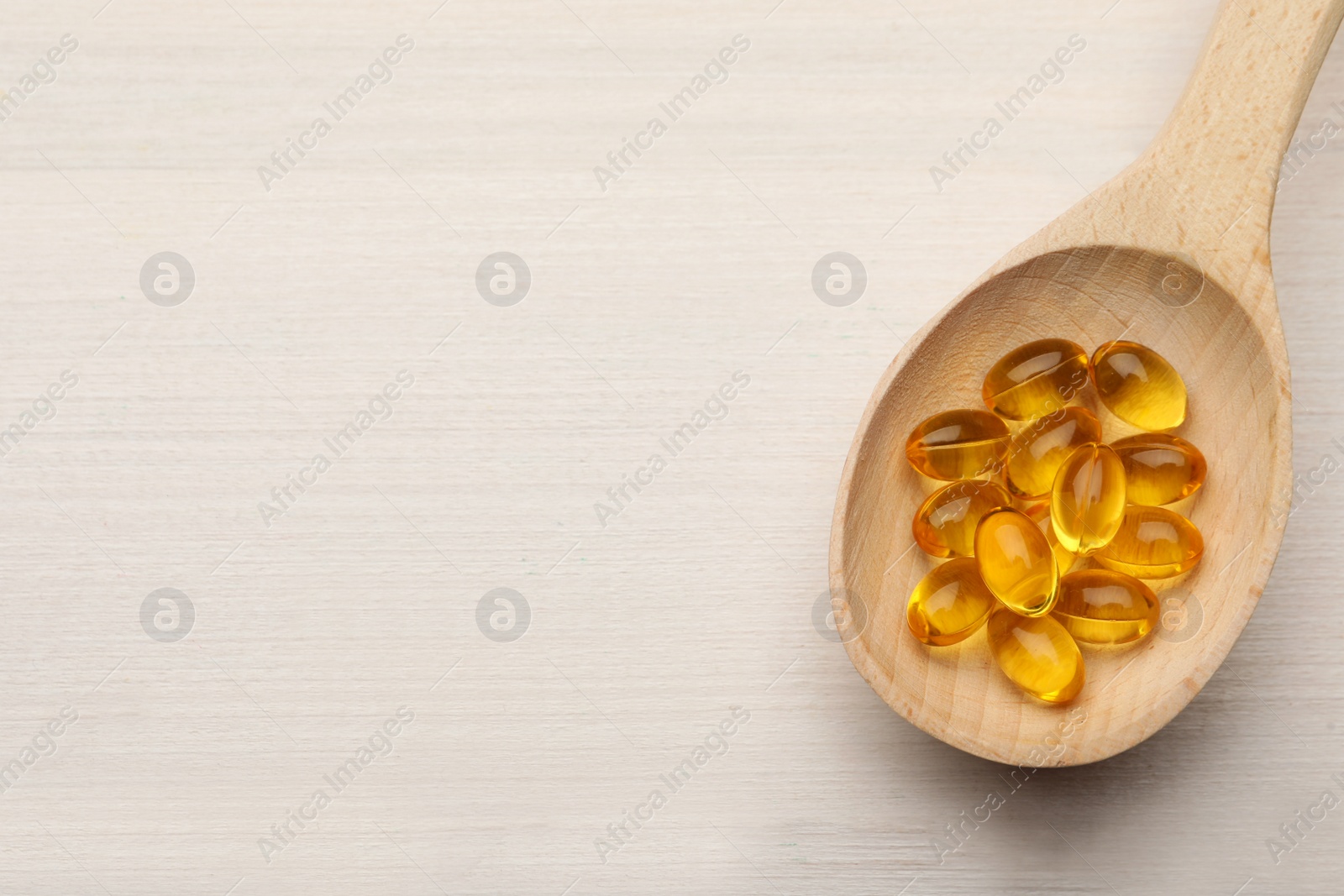 Photo of Spoon with dietary supplement capsules on white wooden table, top view. Space for text