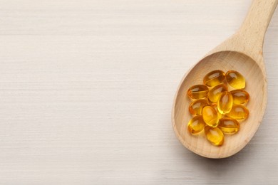 Photo of Spoon with dietary supplement capsules on white wooden table, top view. Space for text