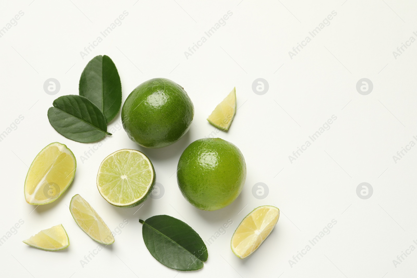 Photo of Whole and cut fresh ripe limes with green leaves on white background, flat lay