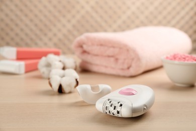 Modern epilator and other hair removal products on wooden table. Space for text