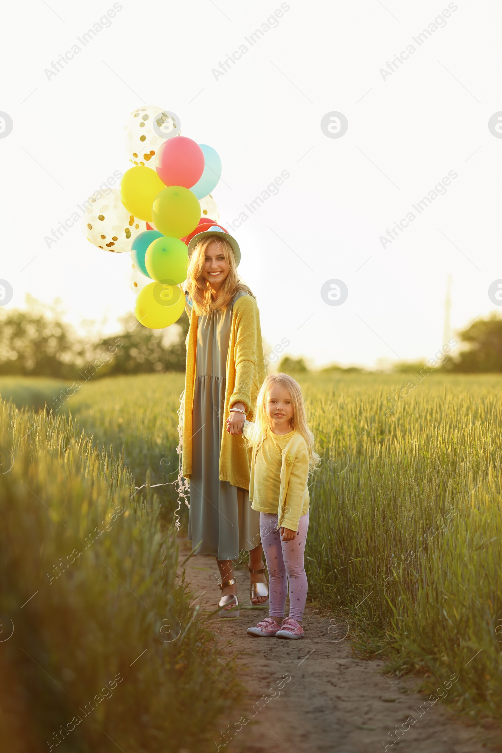 Photo of Young woman and her daughter with colorful balloons in field on sunny day