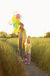 Photo of Young woman and her daughter with colorful balloons in field on sunny day