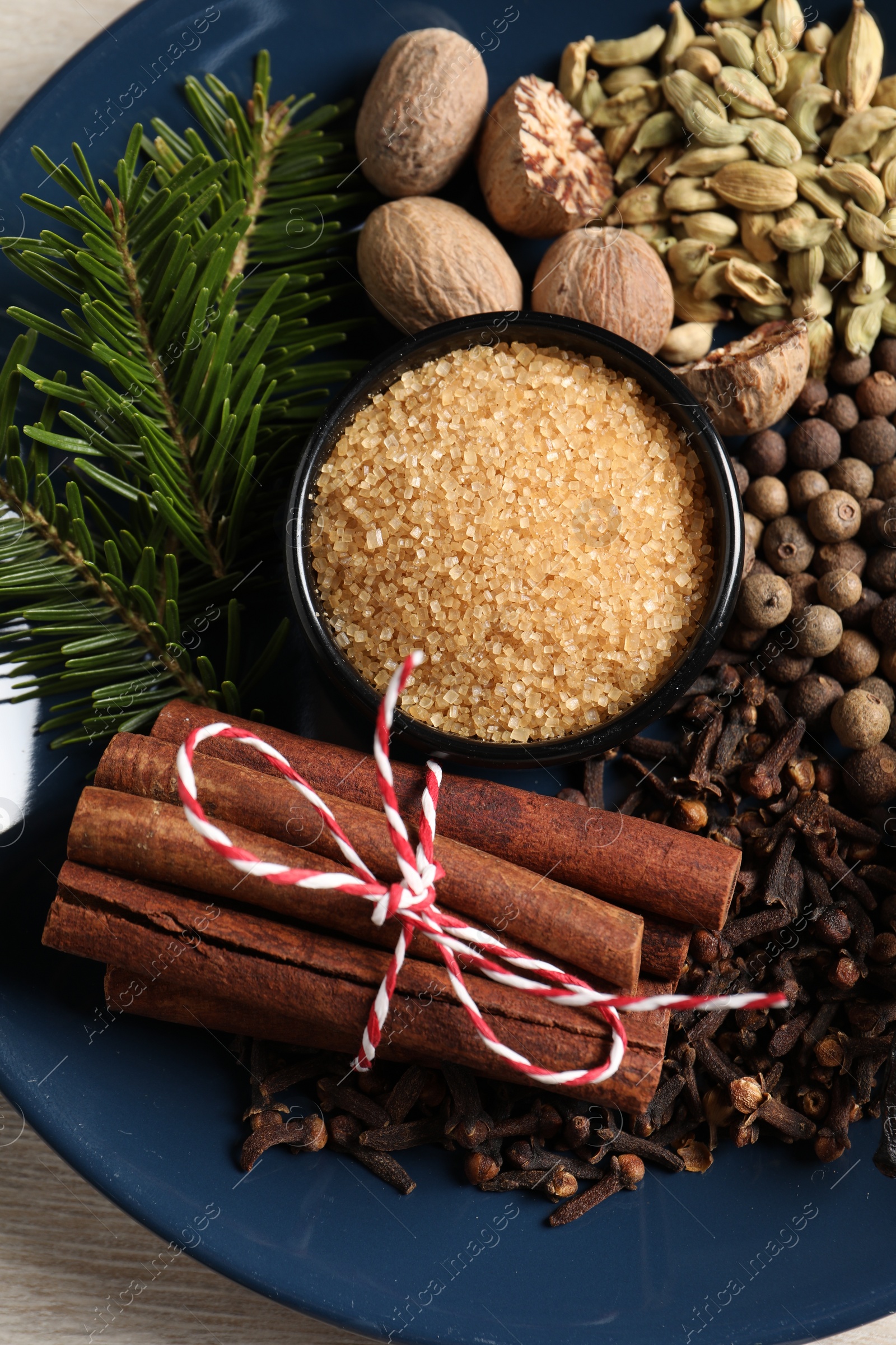 Photo of Plate with different aromatic spices and fir branches on light wooden table, top view