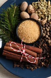 Plate with different aromatic spices and fir branches on light wooden table, top view