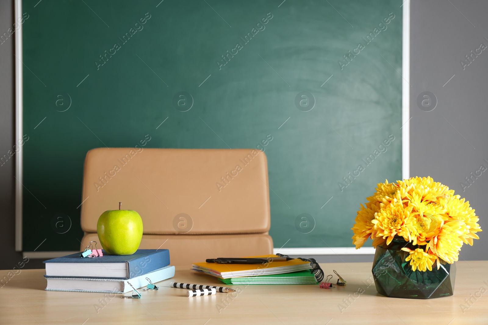 Photo of Bouquet of flowers, apple and notebooks on table in classroom. Teacher day celebration