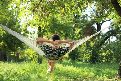 Photo of Young man resting in comfortable hammock at green garden