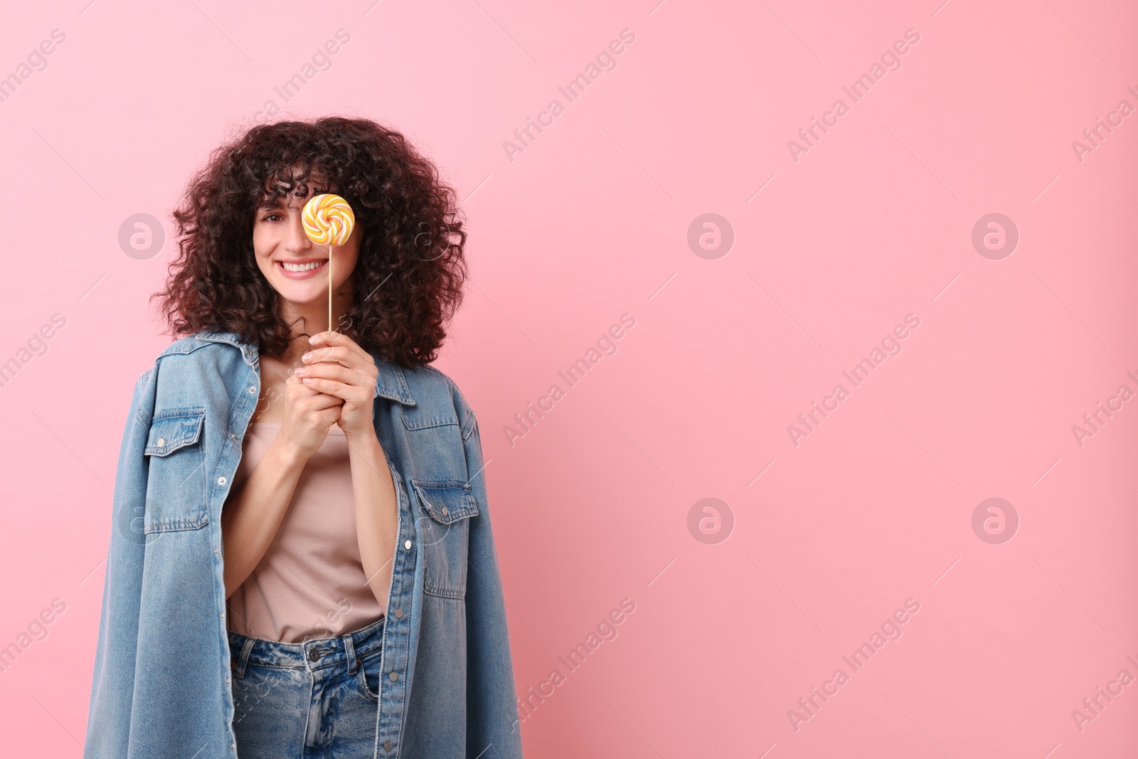 Photo of Beautiful woman covering eye with lollipop on pink background, space for text