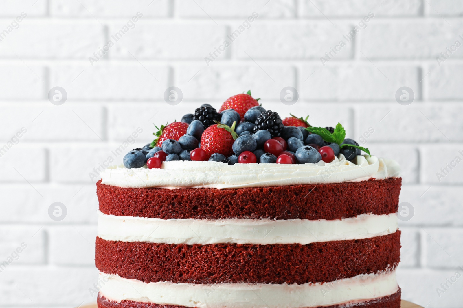 Photo of Delicious homemade red velvet cake with fresh berries near brick wall, closeup